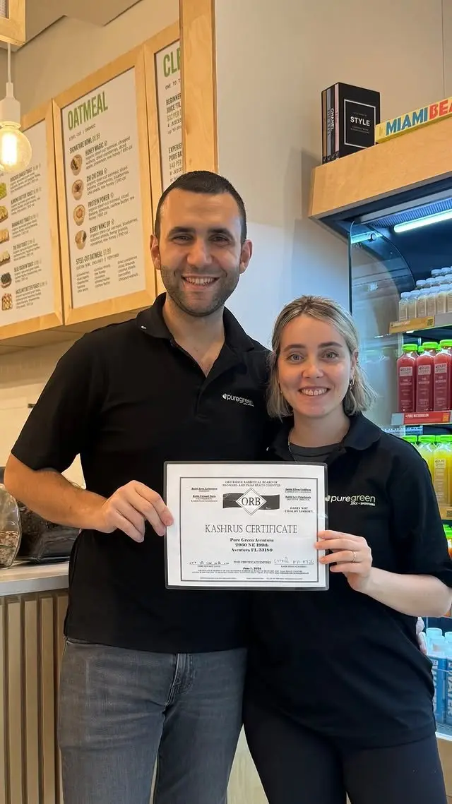Two Pure Green Aventura team members holding the store’s kosher certificate behind the counter