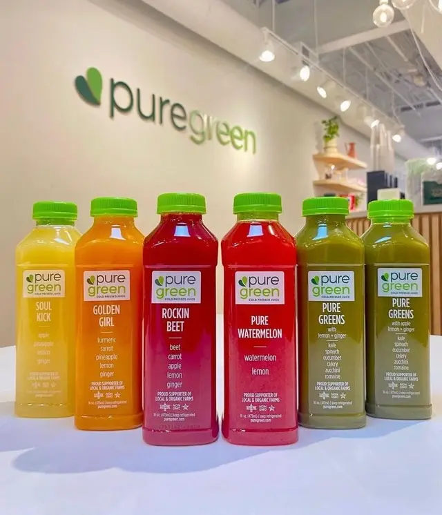 Six cold-pressed juices lined up under the logo wall at Pure Green Columbia