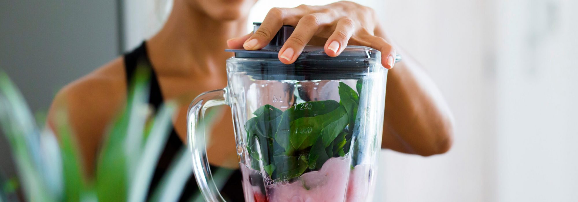 Woman blending spinach, berries, bananas and almond milk to make a healthy green smoothie